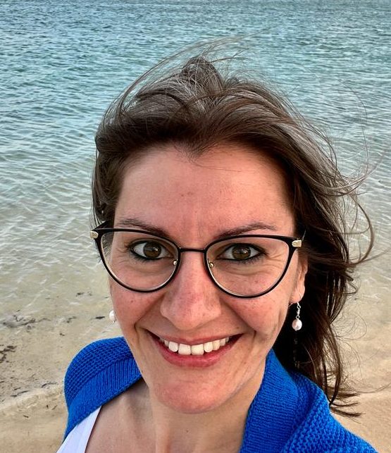 Das bin ich Lächelnde Frau mit Brille und langen Haaren, am Strand vor Wasser.
